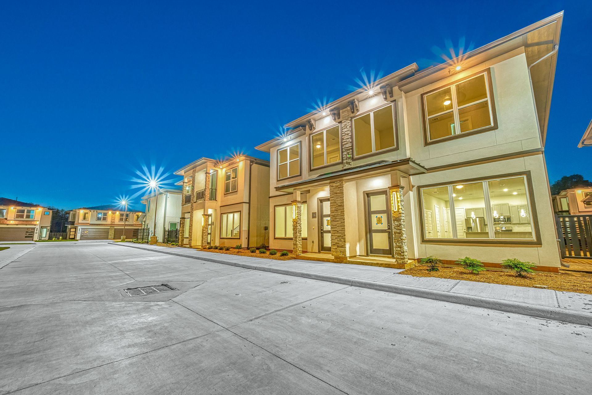 Row of modern townhomes with lit windows along a snowy driveway at dusk