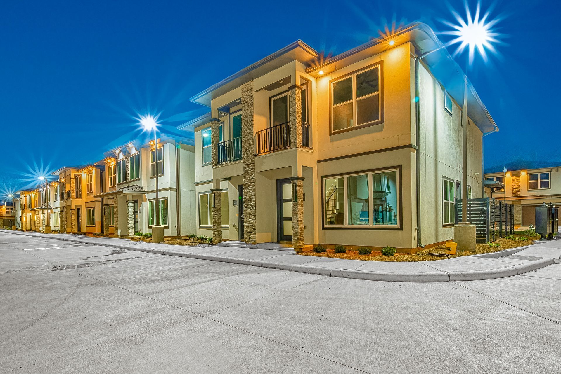 Snow-covered row of modern townhouses lit by bright streetlights at dusk