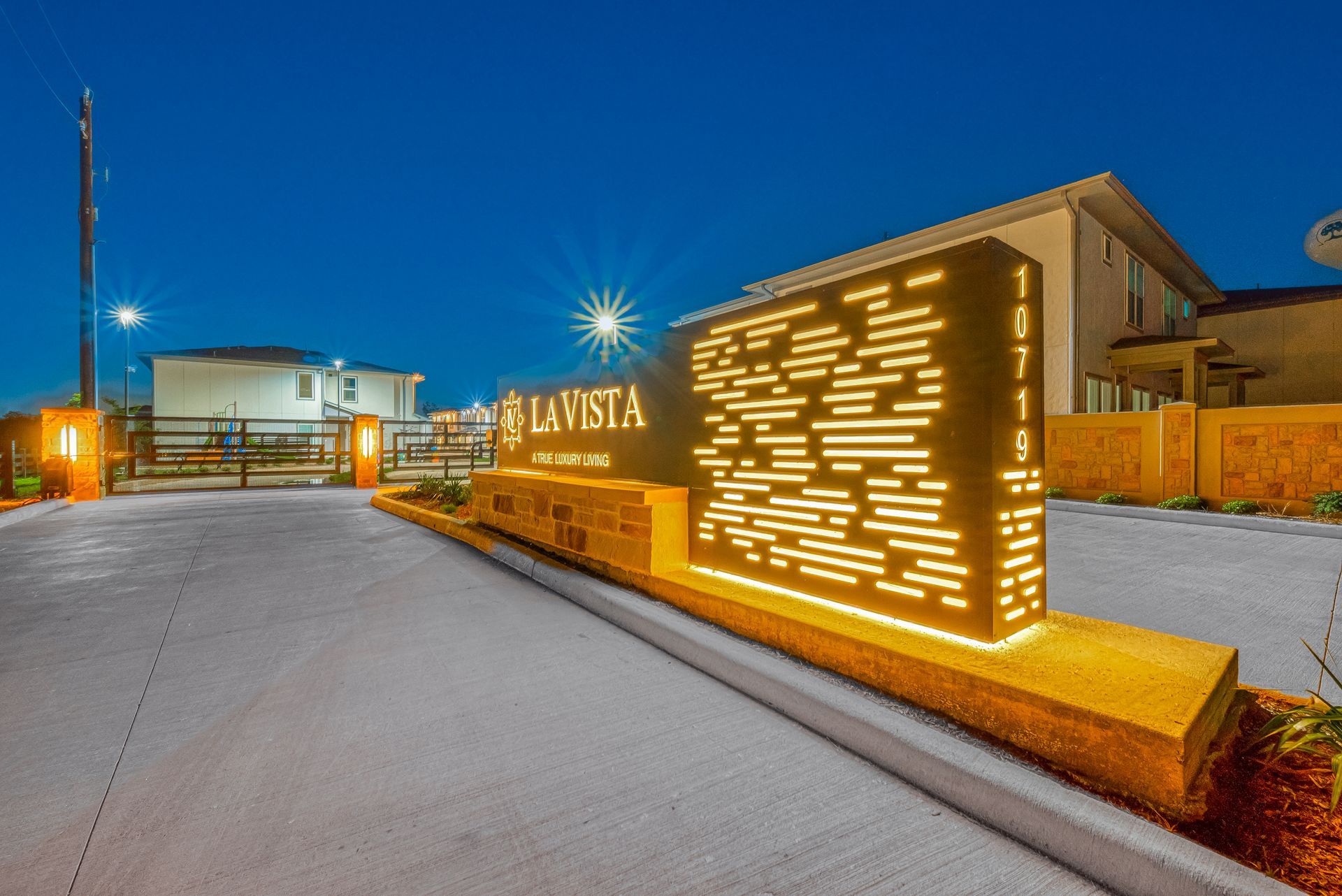 Illuminated sign for La Vista at dusk beside a modern building and gravel driveway