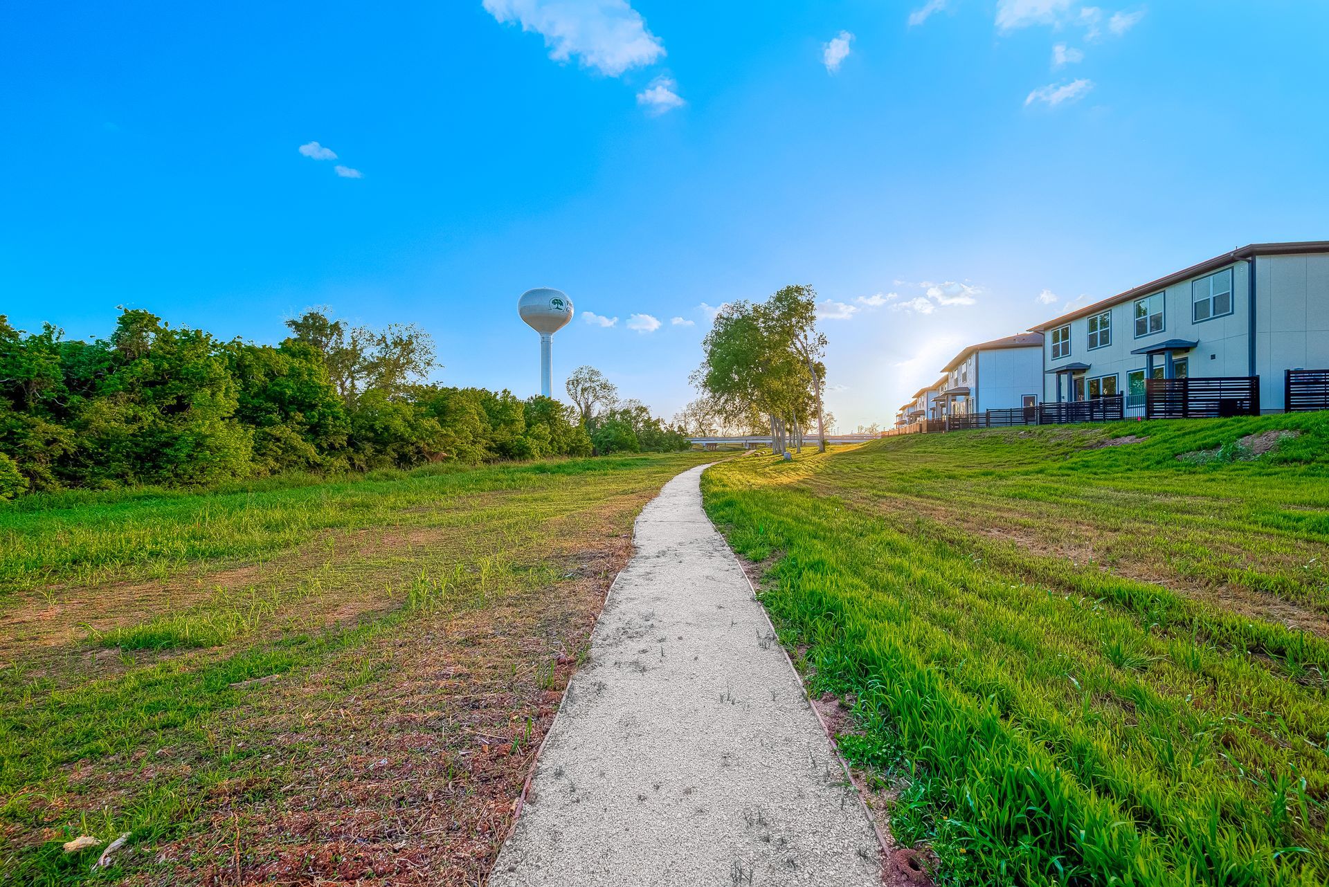 Gravel path through a grassy field toward buildings under a blue sky at sunset