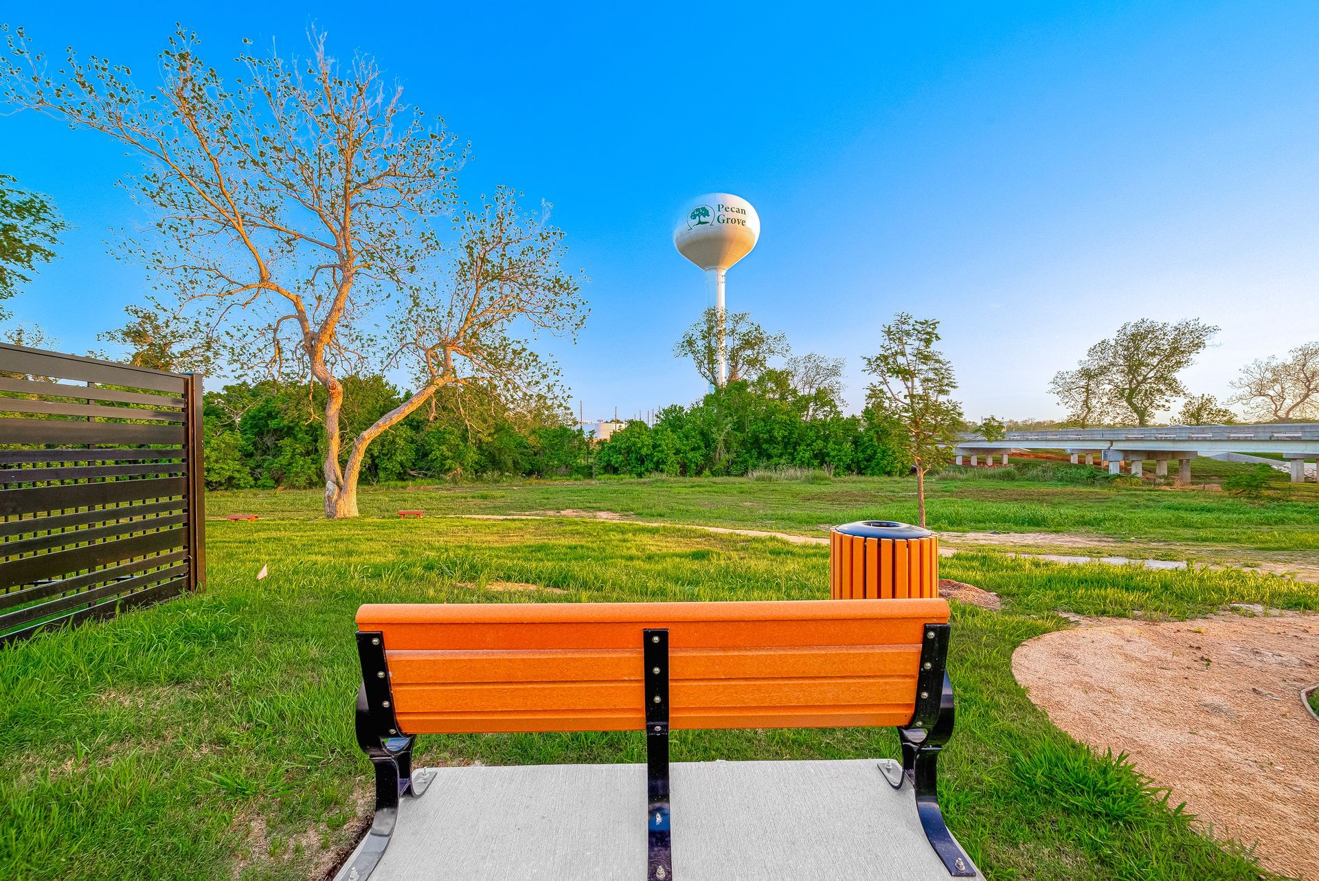 Orange park bench facing a grassy field with trees, a water tower, and a clear blue sky