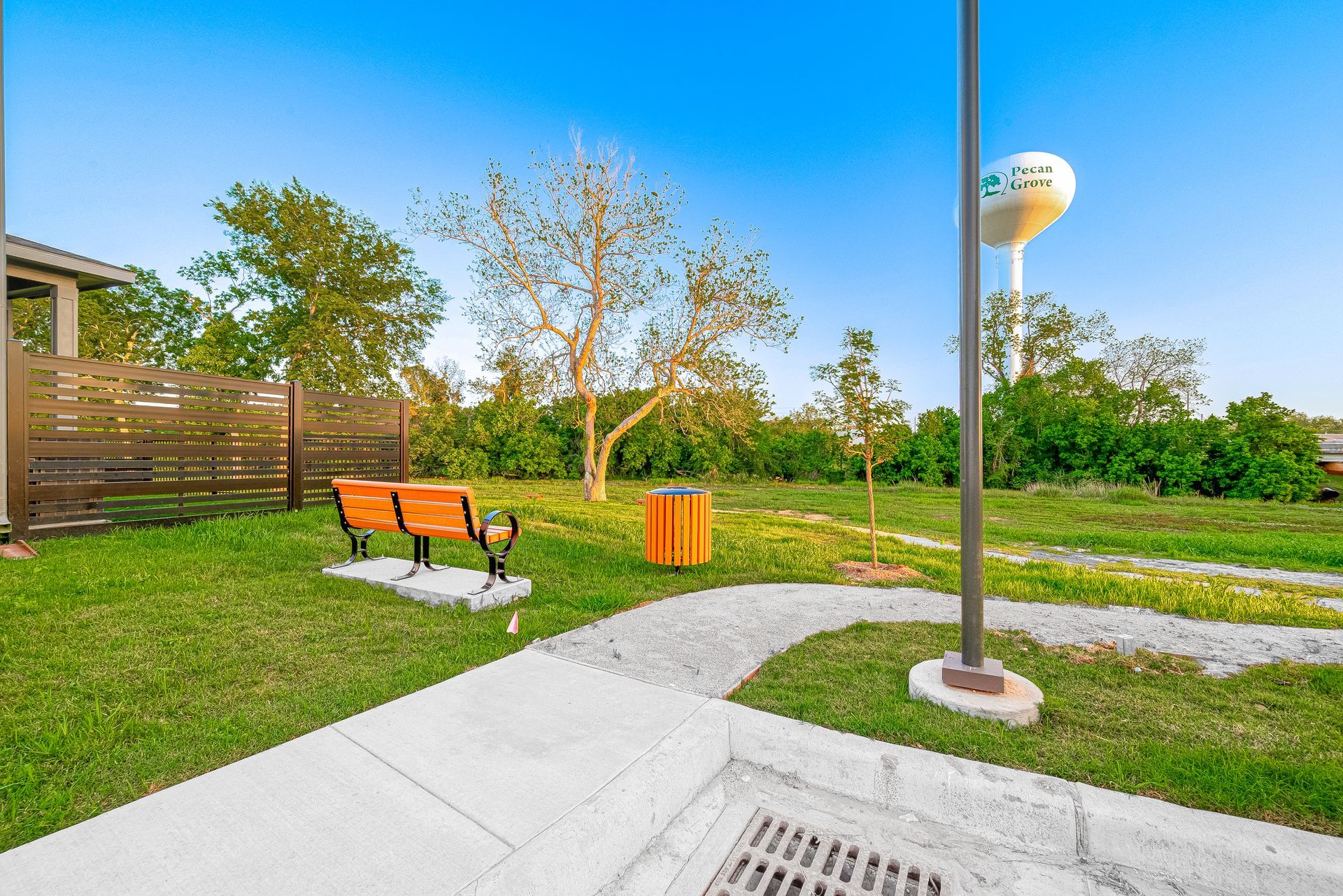 Sunny park with orange bench, grassy lawn, and a paved path under blue sky