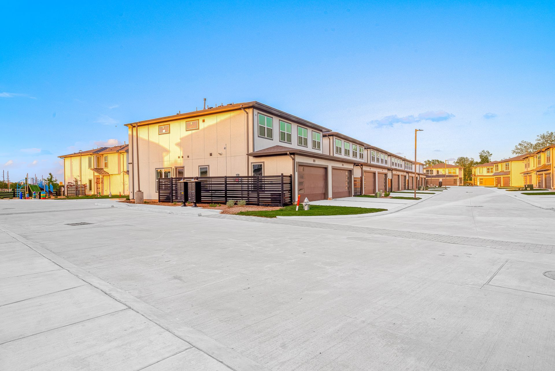 Wide view of a beige two-story building with a large empty paved lot under a blue sky.