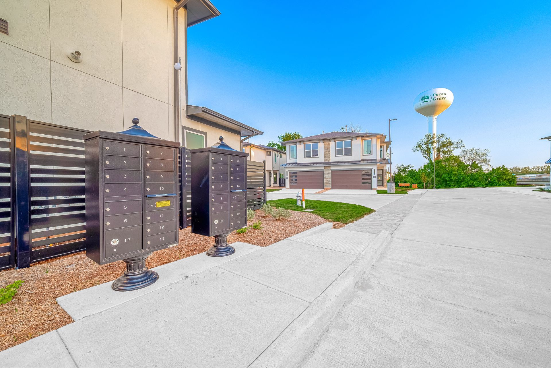 Apartment complex walkway with black utility boxes, paved driveway, and a water tower in the background