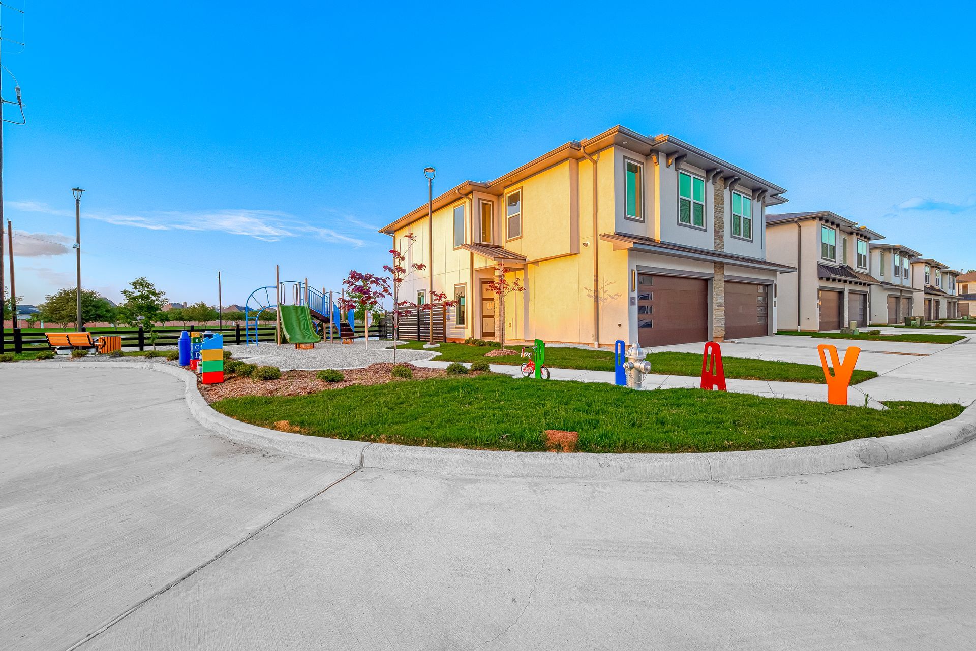 New townhouses with garages on a curved suburban street under a bright blue sky