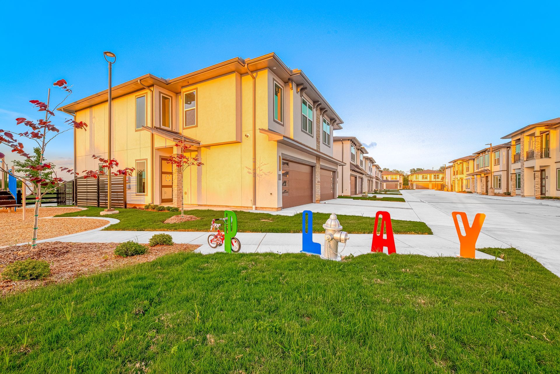 Colorful letters on a grassy lawn in front of tan townhouses on a sunny street
