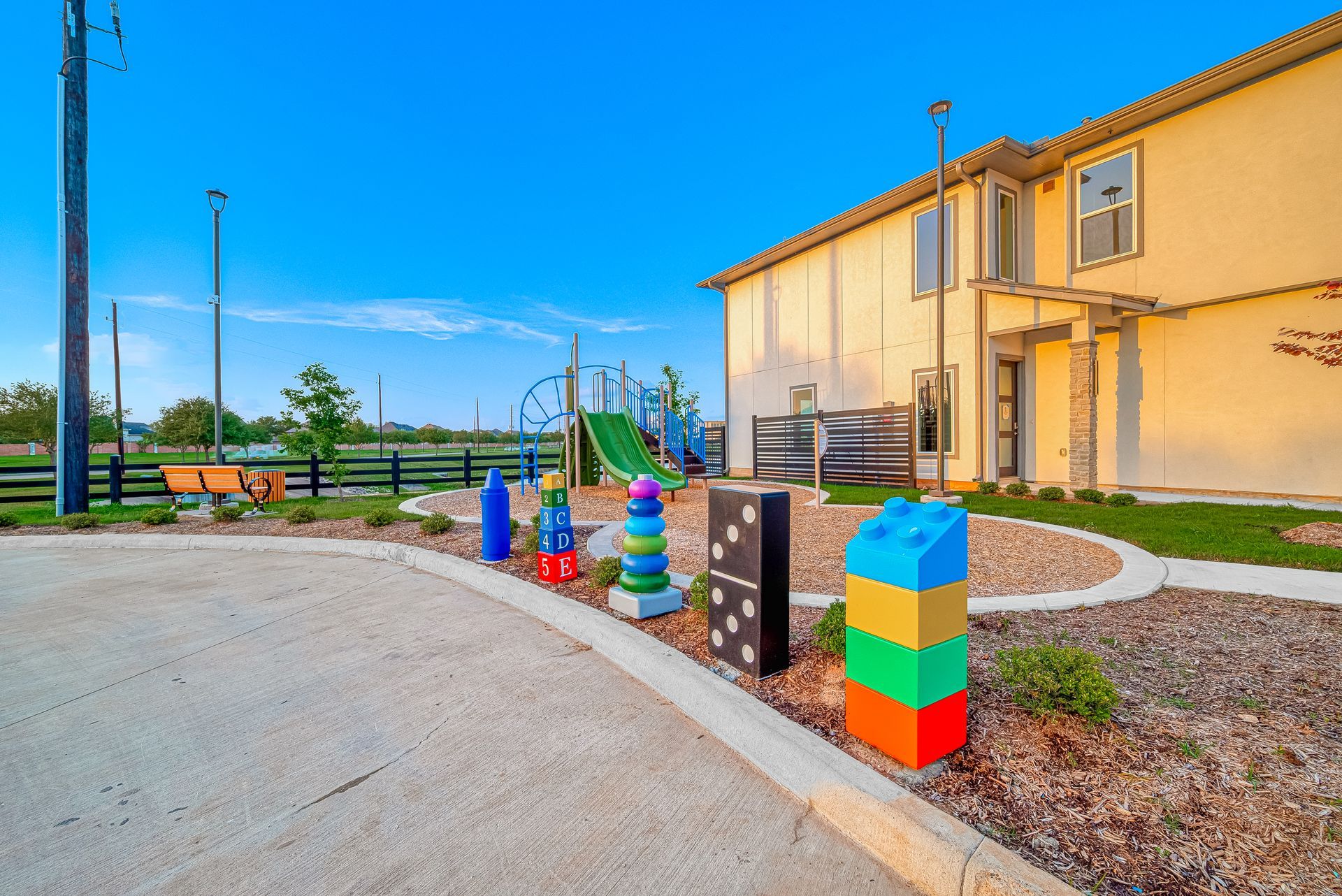 Colorful playground blocks and benches beside a tan building under a bright blue sky.
