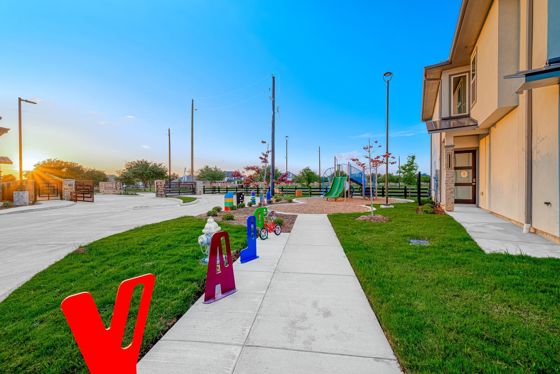 Colorful sculptures along a sidewalk in a grassy plaza at sunset