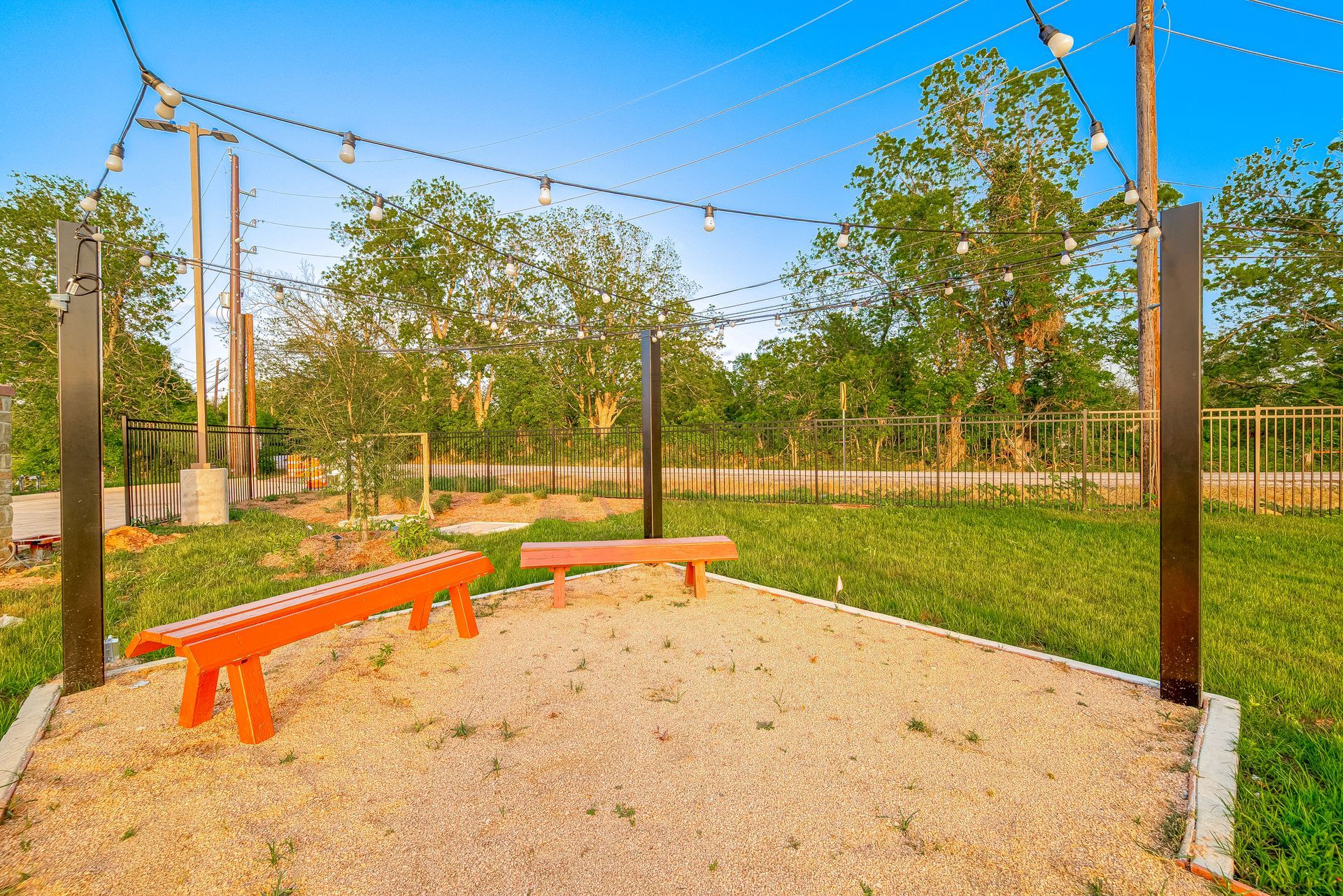 Outdoor gravel seating area with orange benches, string lights, and trees in a park-like setting
