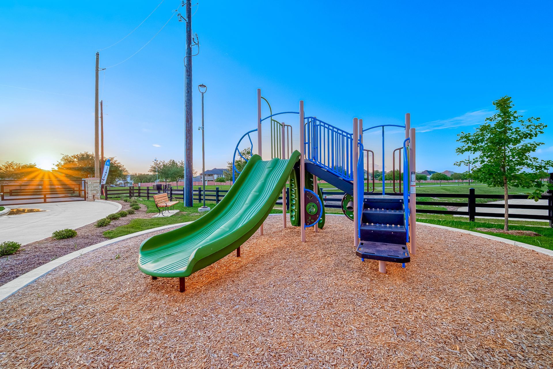 Playground with green slide and blue stairs on a woodchip surface at sunset