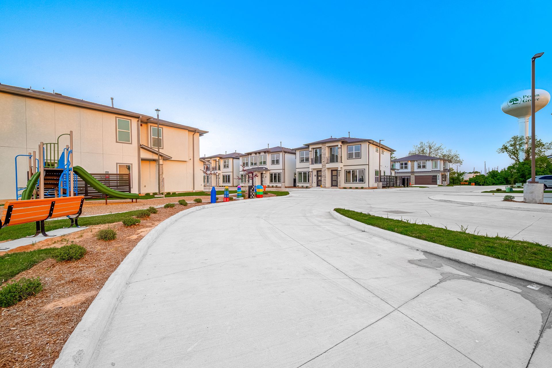 Residential courtyard with playground, apartment buildings, and a curved concrete driveway under a blue sky