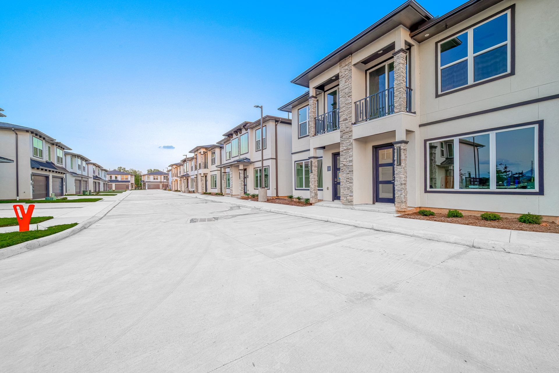 Row of modern beige townhouses on a quiet residential street under a blue sky