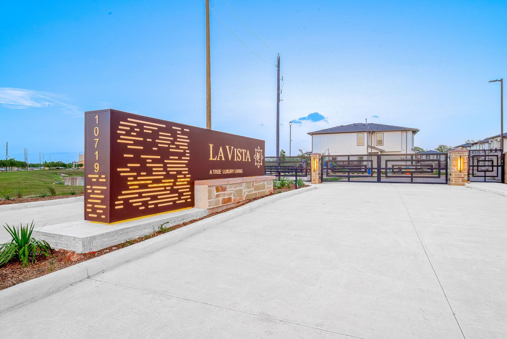 Entrance sign and gated driveway to a modern facility under a bright blue sky.
