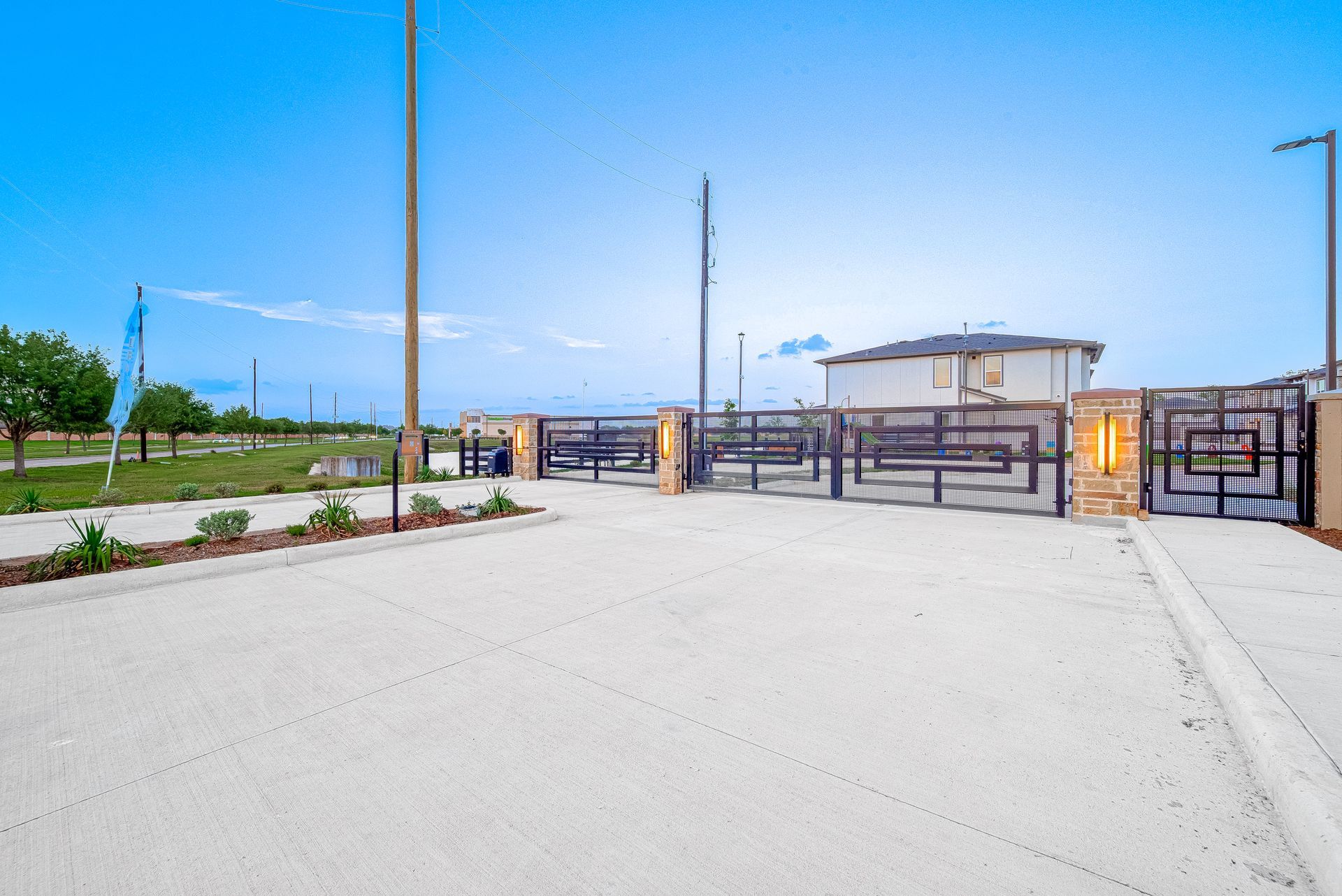 Gated entrance to a modern building with a wide paved driveway and landscaping under a clear blue sky