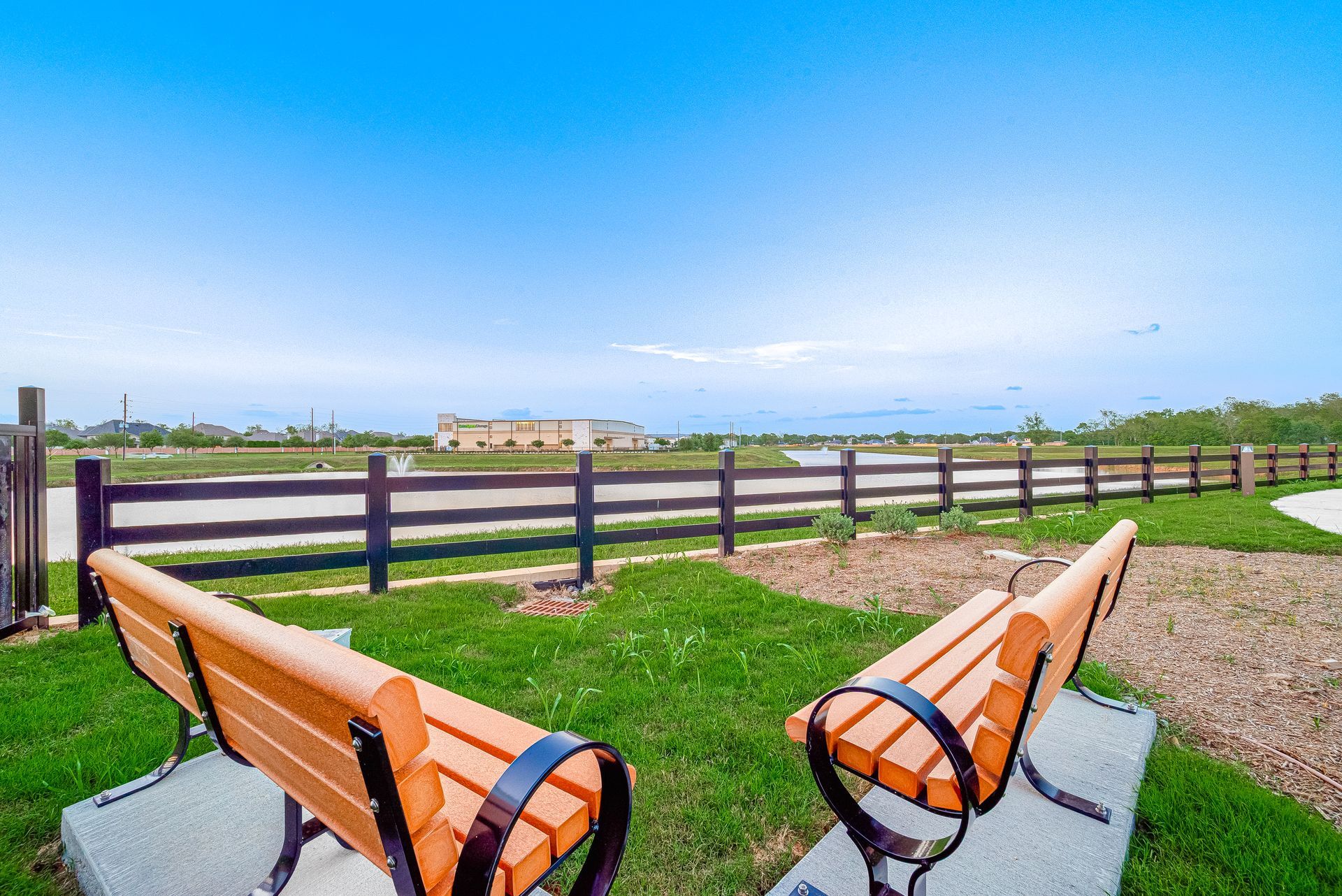 Two wooden benches facing a green field under a clear blue sky.