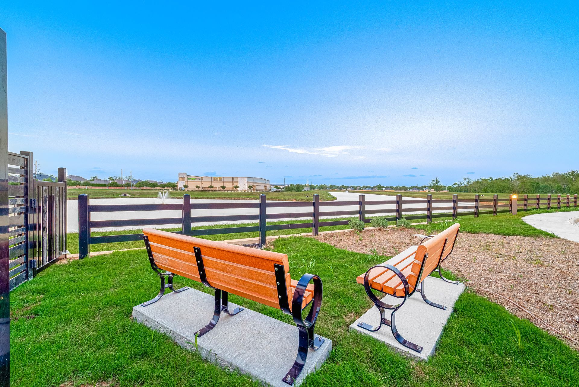 Two orange benches overlooking a green field with a wooden fence and blue sky