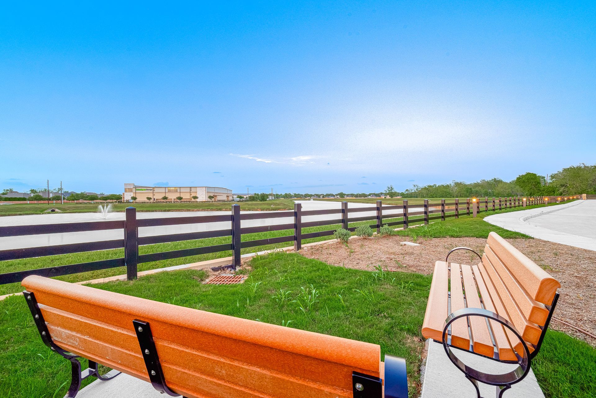 Park bench overlooking a green field and fence under a clear blue sky