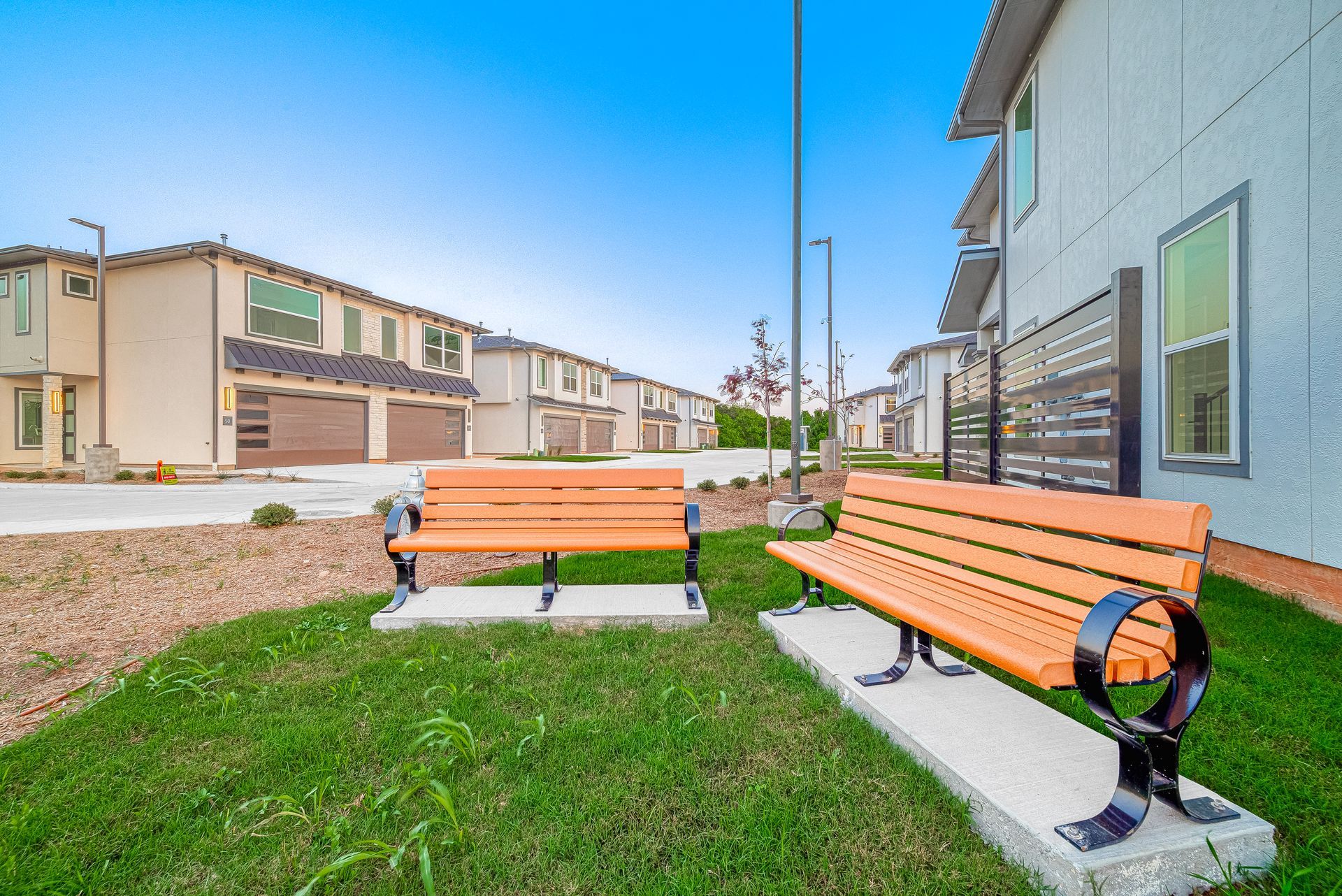 Two orange benches on a grassy patio beside apartment buildings under a blue sky