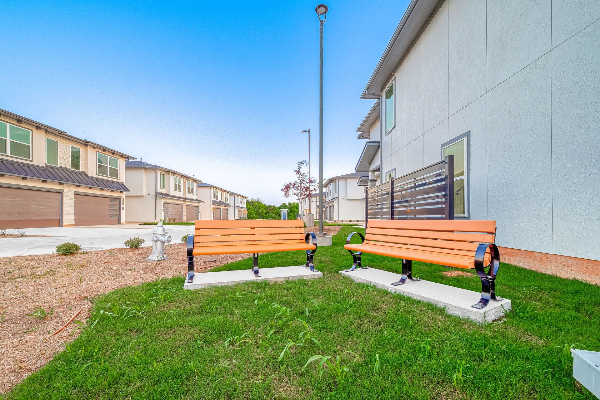 Two wooden benches on a grassy courtyard beside a building and apartment rowhouses under a clear sky
