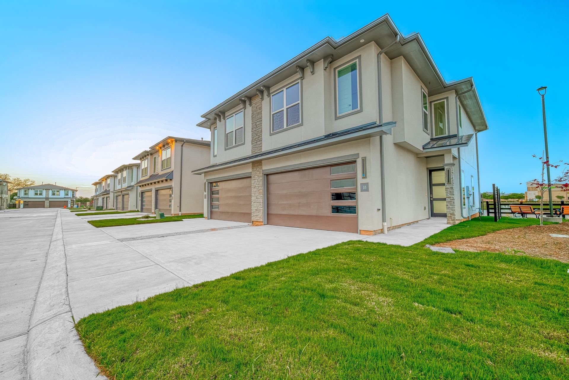 Suburban row of modern beige townhouses with garages beside a green lawn under a blue sky