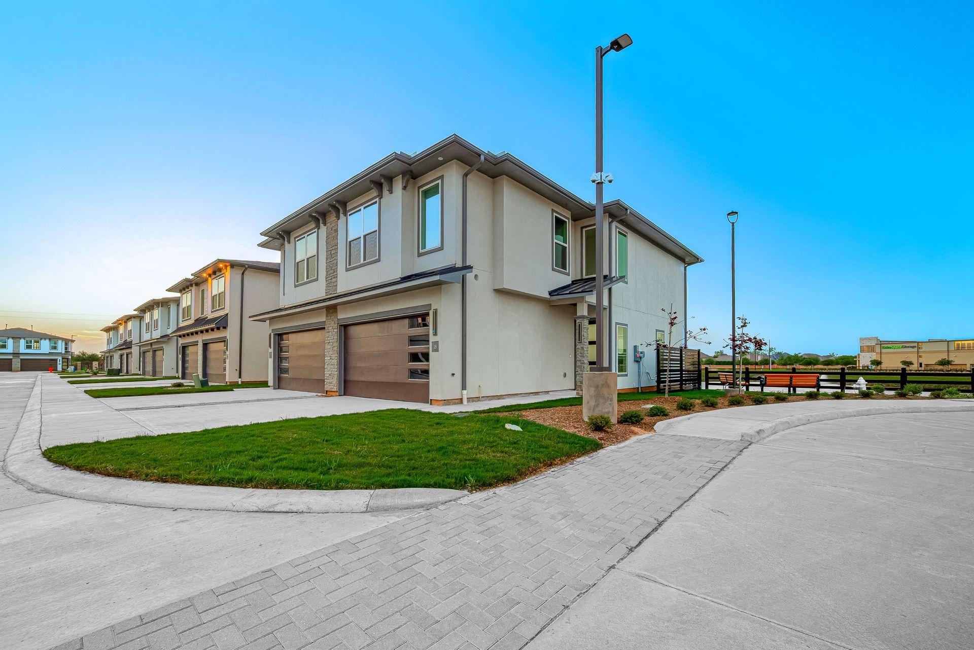 Row of modern beige townhouses with garages along a quiet street under a clear blue sky