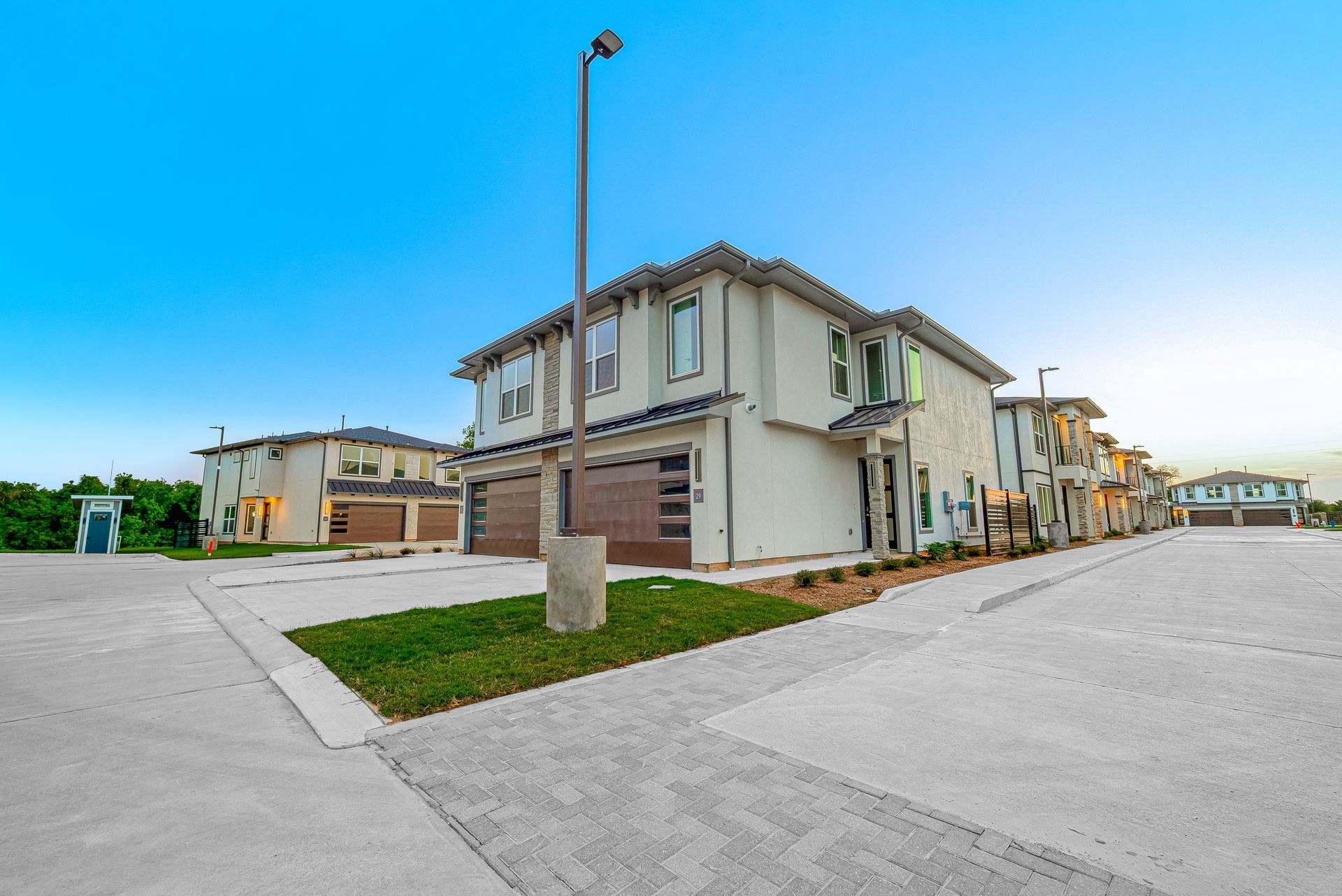 Modern townhouse corner lot with a streetlamp and paved driveway under a blue sky