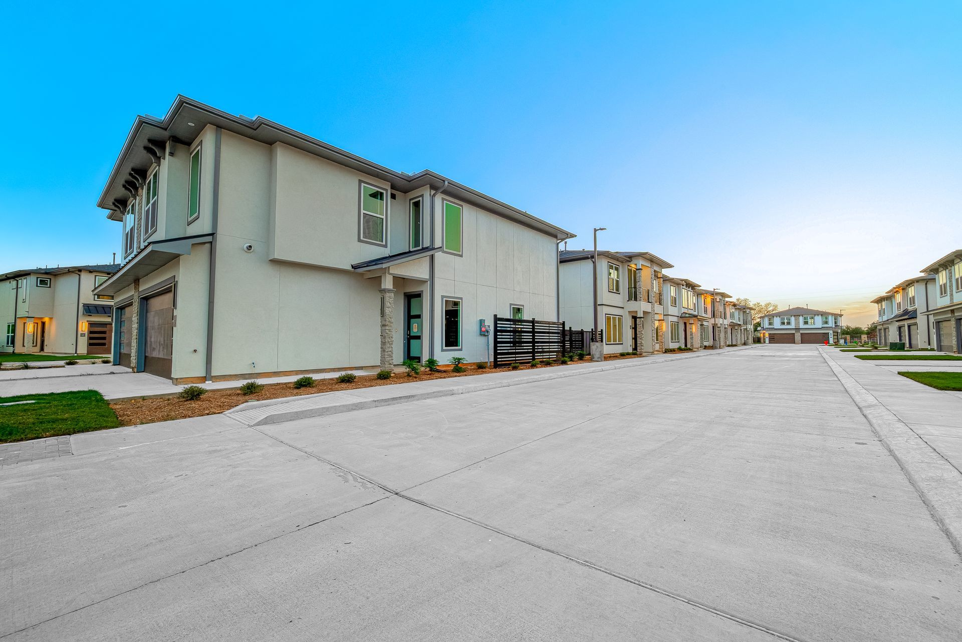 Suburban apartment complex with rows of beige townhomes along a wide paved street under a blue sky