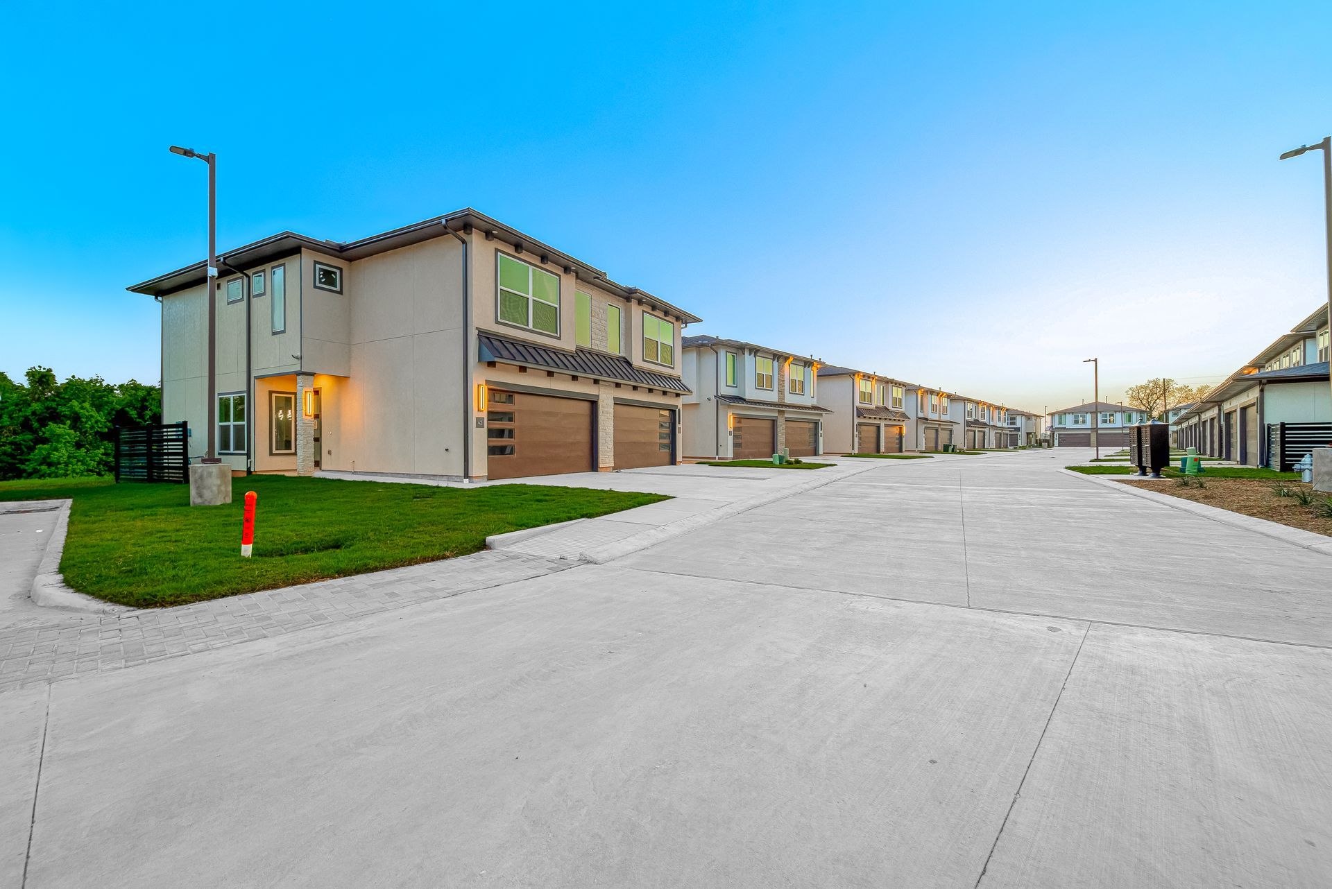Modern apartment complex with beige buildings and a wide empty driveway at dusk
