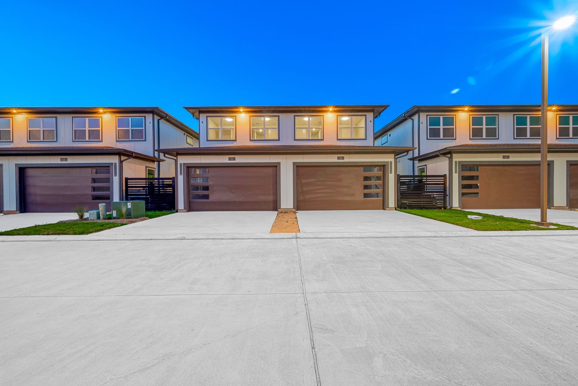 Row of modern townhouses with lit windows and double garages at dusk
