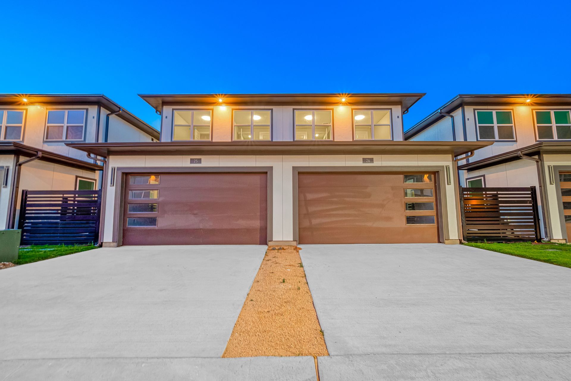 Modern townhouse duplex with two garage doors, concrete driveway, and blue evening sky