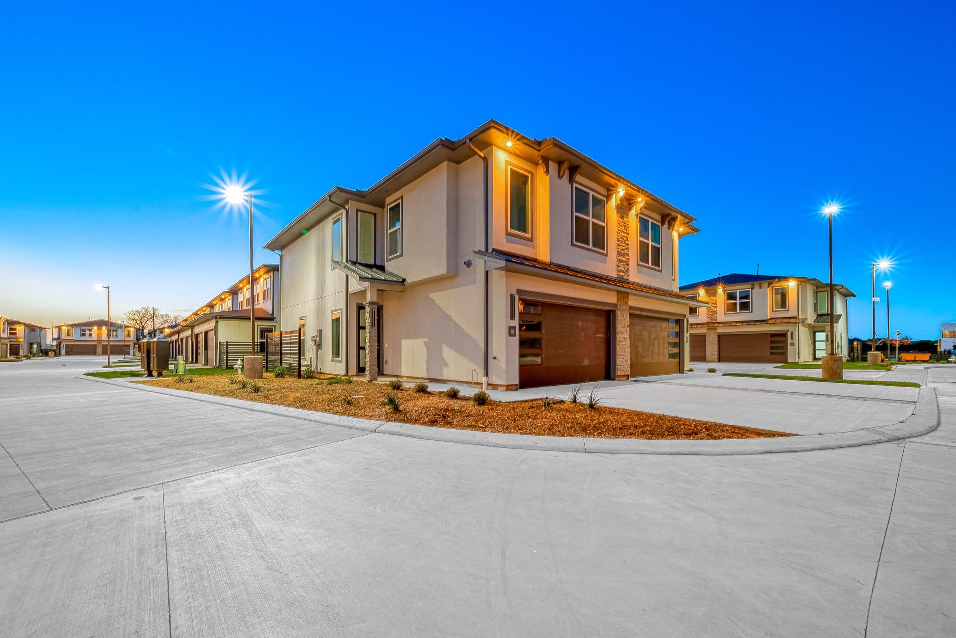 Modern two-story suburban house at dusk with a garage, lit windows, and a quiet street corner