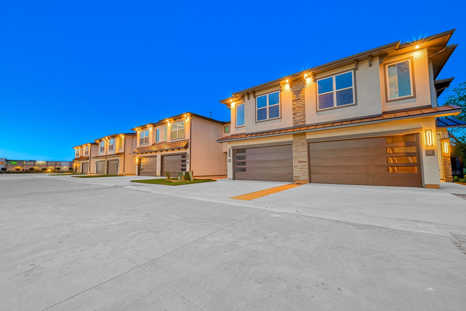 Row of modern beige townhouses with garages at dusk on a wide paved street