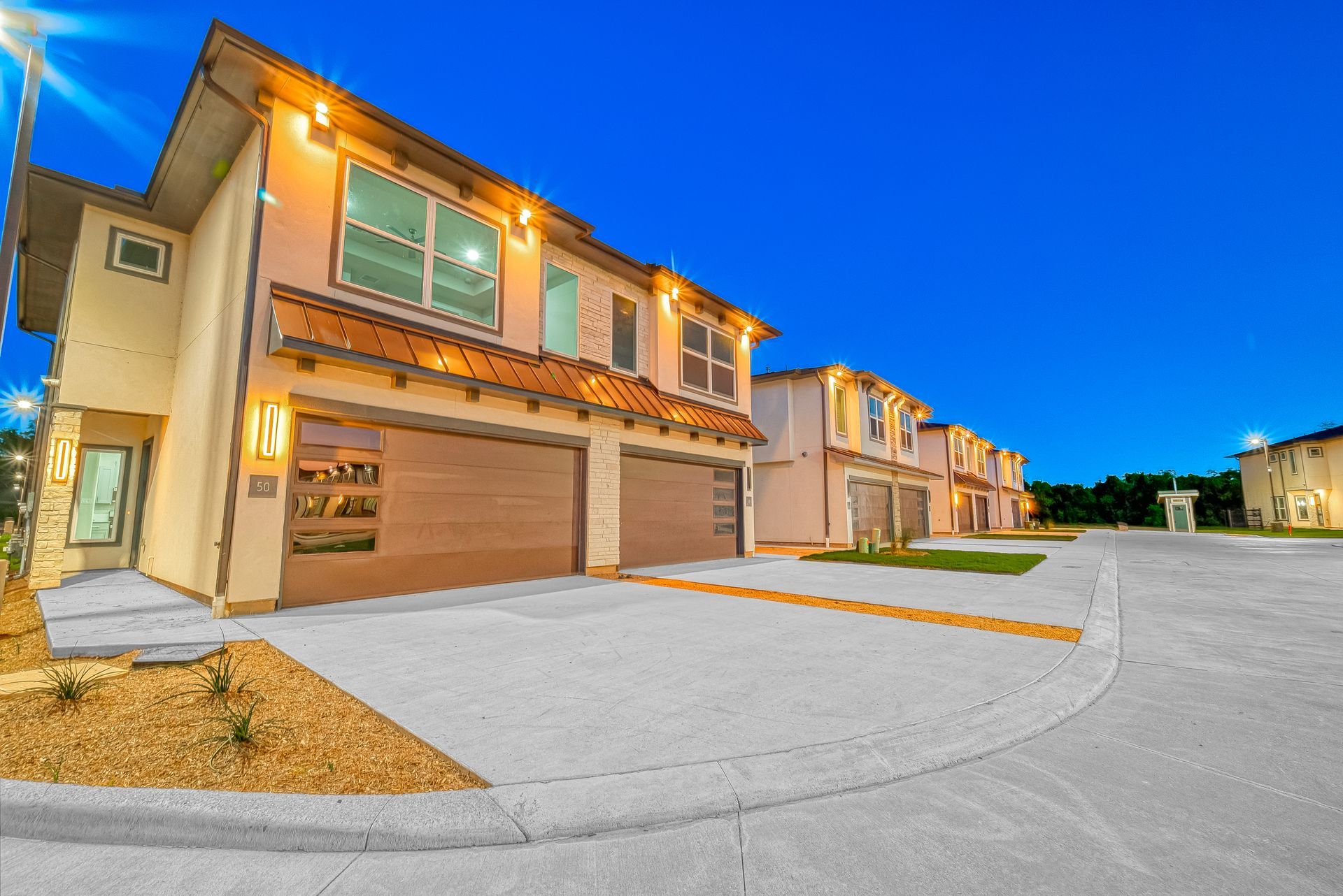 Modern two-story townhomes with garages along a quiet paved street at dusk
