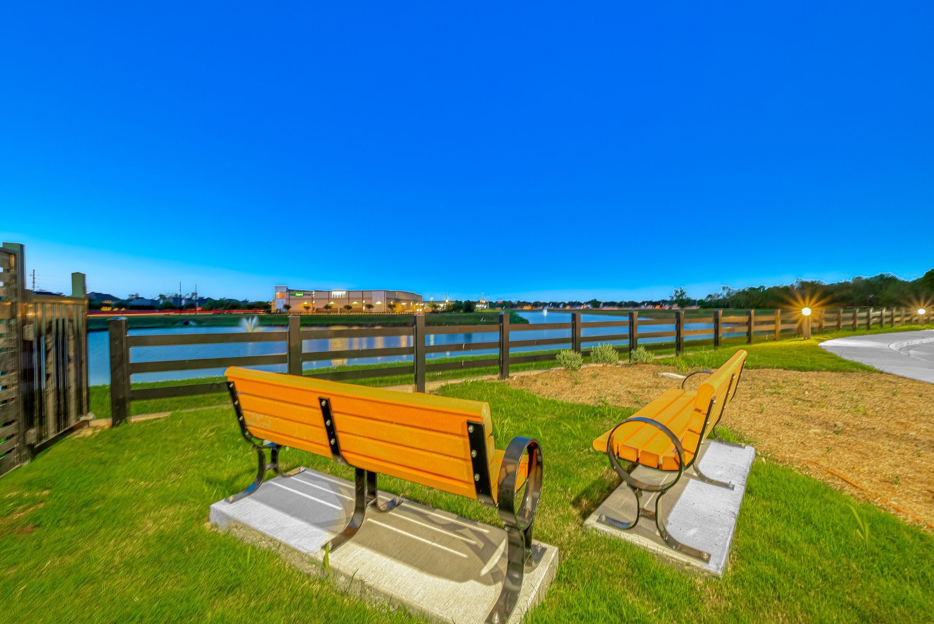 Two orange benches on a grassy waterfront park at dusk, facing a river and distant buildings