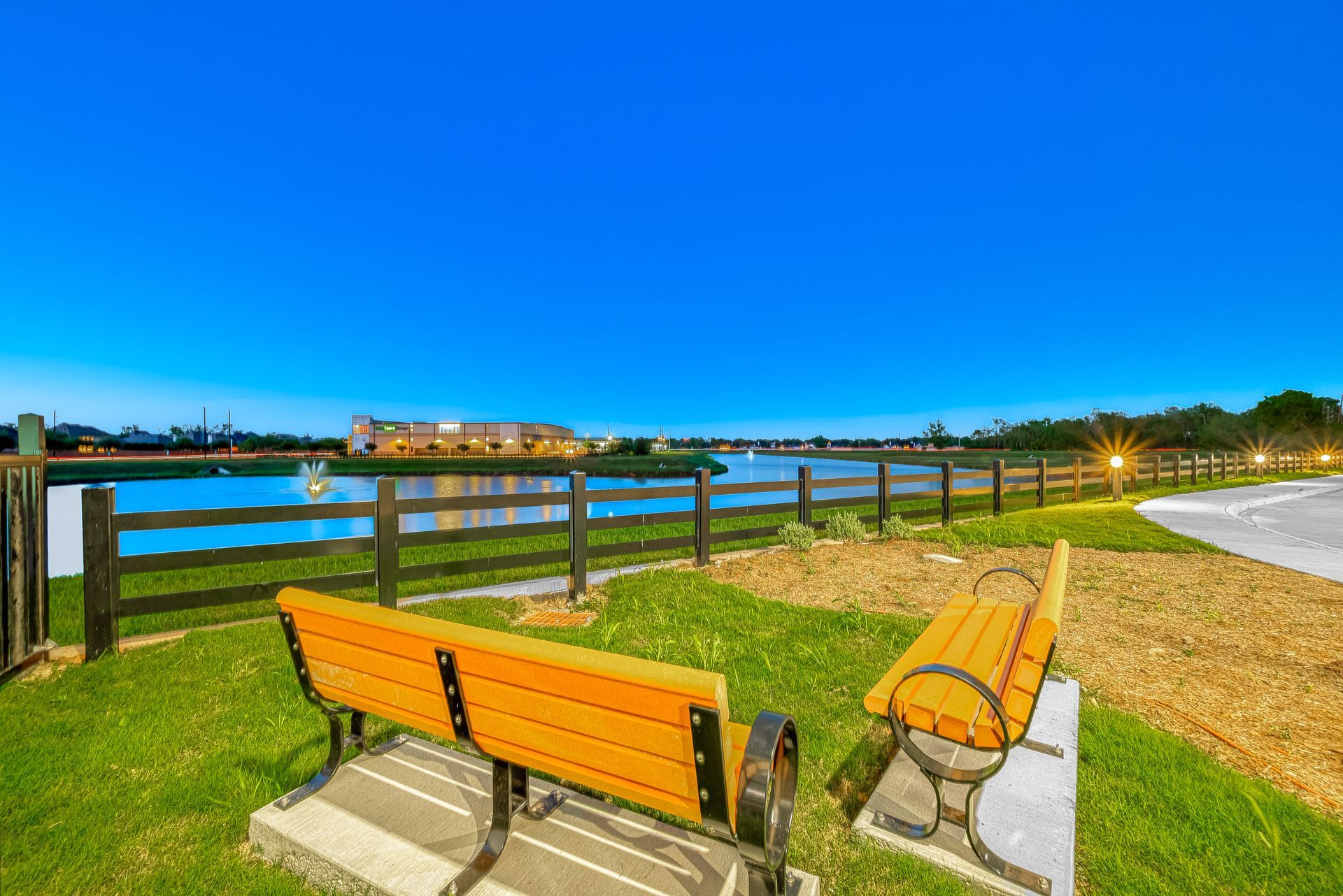 Wooden benches beside a river at sunset, with a blue sky and distant shoreline lights
