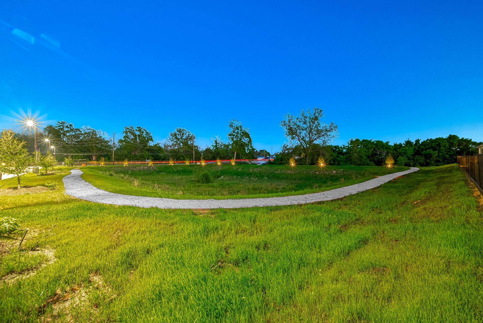 Curved white path through a green park at dusk under a bright blue sky