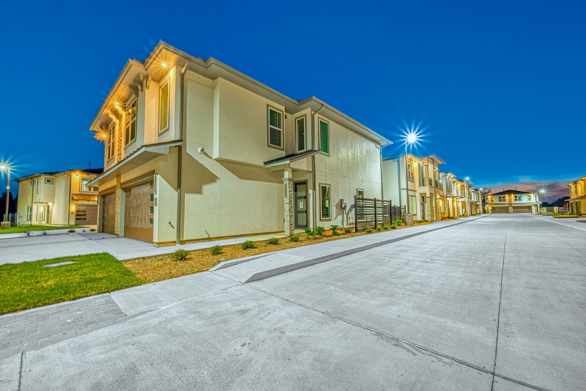 Modern townhouse row at dusk with lit streetlights and empty paved street
