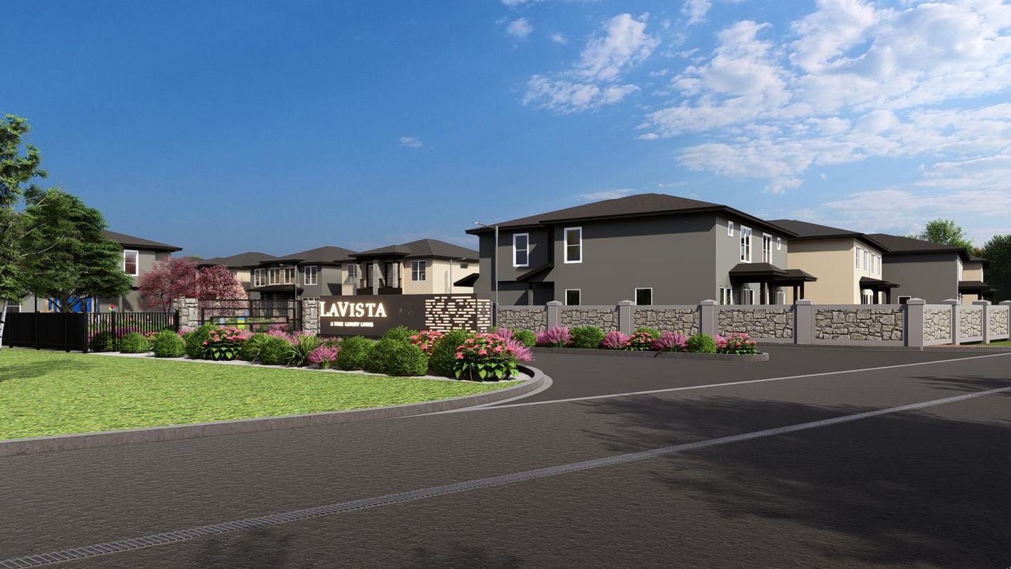 Modern apartment complex with landscaped entrance, red flowers, and parking lot under a blue sky