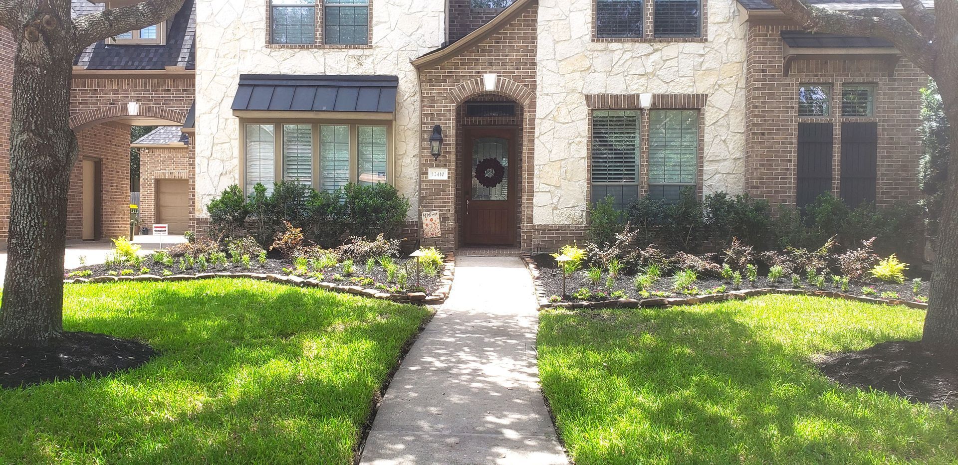 Brick townhouse with a front walkway, green lawn, and landscaped flower beds in daylight