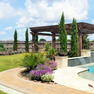 Poolside pergola with cypress trees, landscaping, and water feature.