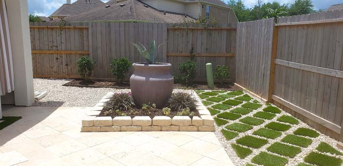 Backyard patio with large pot in the middle and a walkway with green grass inserts.