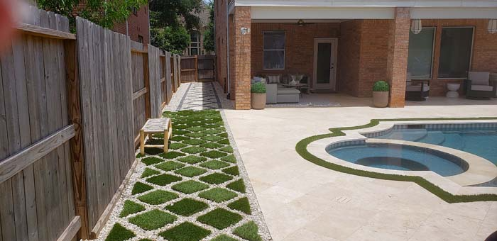 Backyard with a pool, patio, wooden fence, and diamond-patterned grass and gravel pathway.