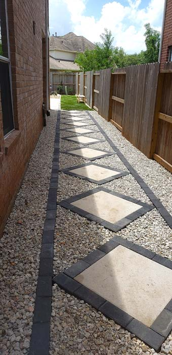 A narrow walkway between a brick building and a wooden fence, featuring diamond-shaped stepping stones.