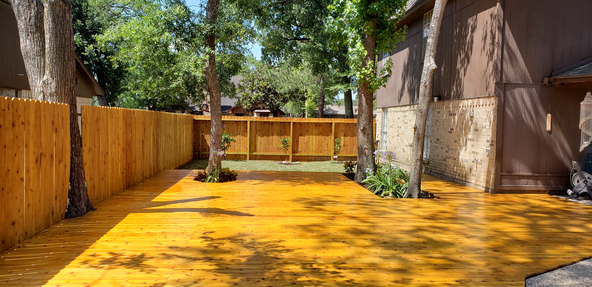 Wooden deck in a backyard with trees and a wooden fence.