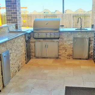 Outdoor kitchen with stainless steel grill, cabinets, sink, and stone countertops.
