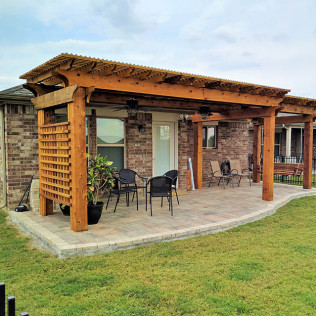 Patio with a wooden pergola, brick wall, pavers, furniture, and a grassy lawn.