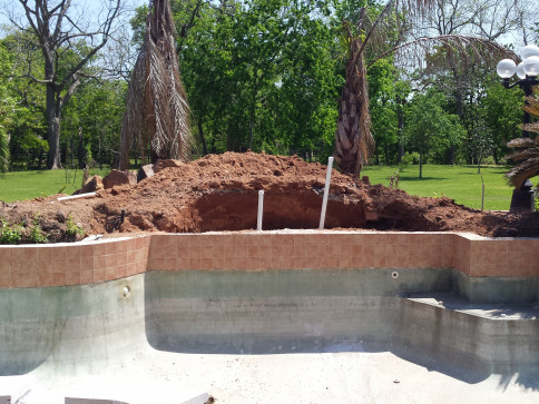 Empty pool with dirt mound in the background, landscaping work in progress.