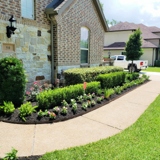 Landscaped front yard with sidewalk, shrubs, flowers, and a brick house.