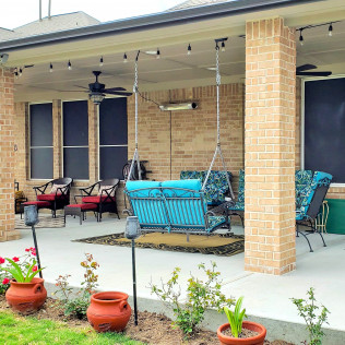 Patio with swing, seating, string lights, and brick pillars. Sunny day.