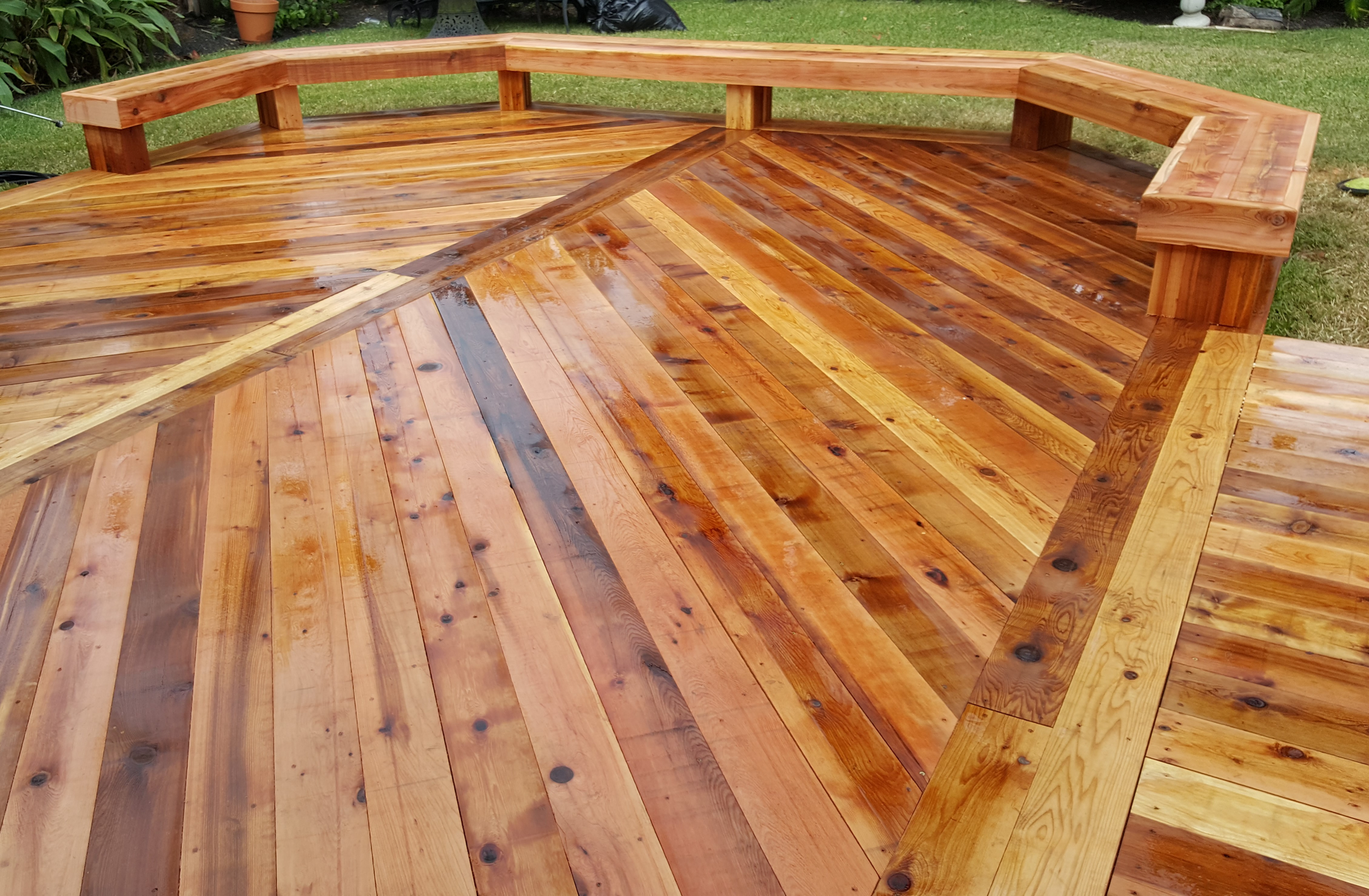 Wooden deck with built-in bench, boards arranged in patterns. Outside, possibly recently stained.